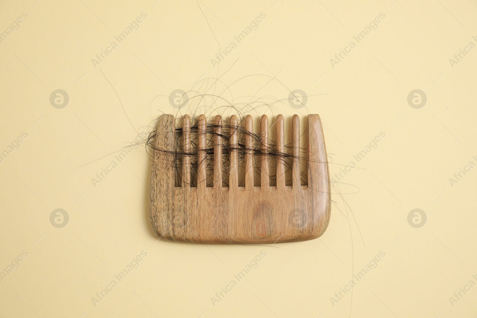 Photo of Wooden comb with lost hair on beige background, top view