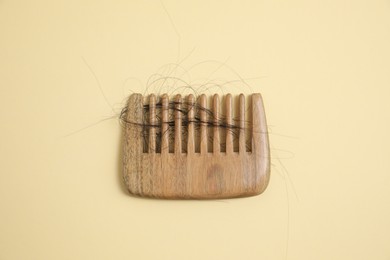Photo of Wooden comb with lost hair on beige background, top view