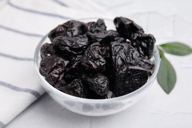 Sweet dried prunes in bowl on light table, closeup