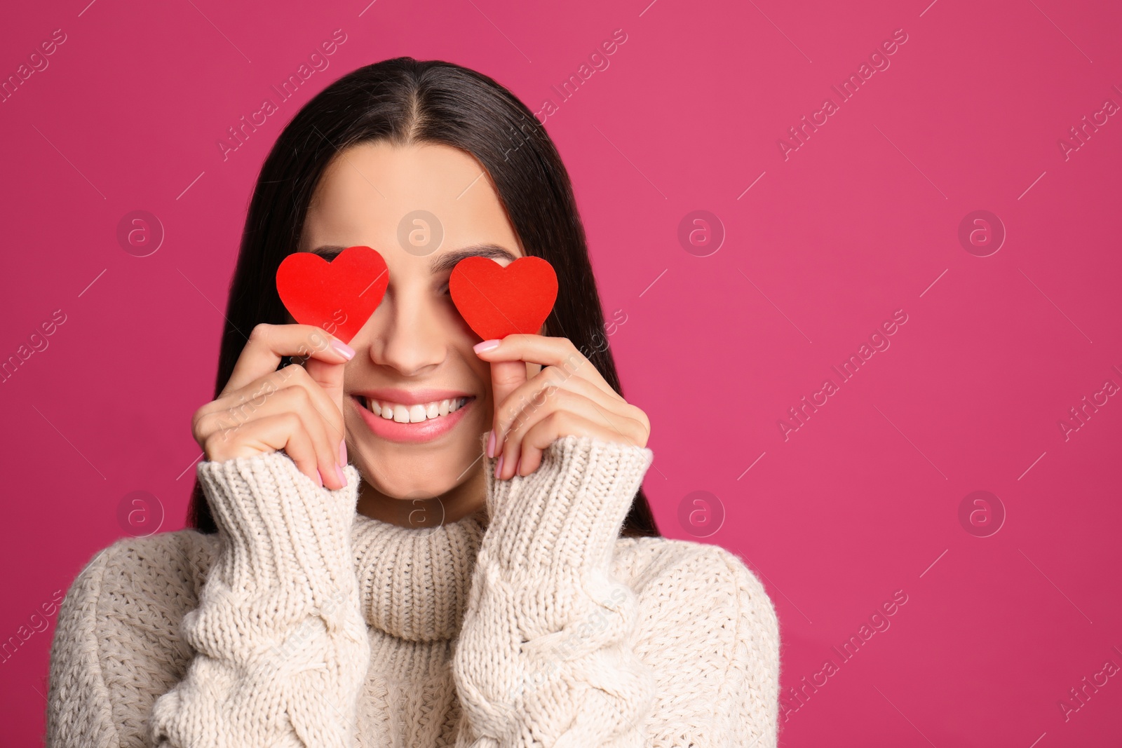 Photo of Portrait of young woman holding paper hearts near eyes on color background. Space for text