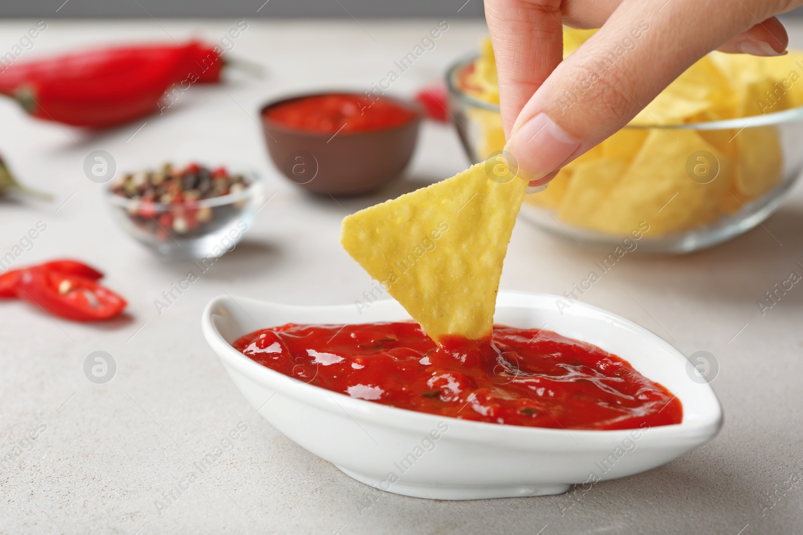 Photo of Woman dipping chip into hot chili sauce in gravy boat on table