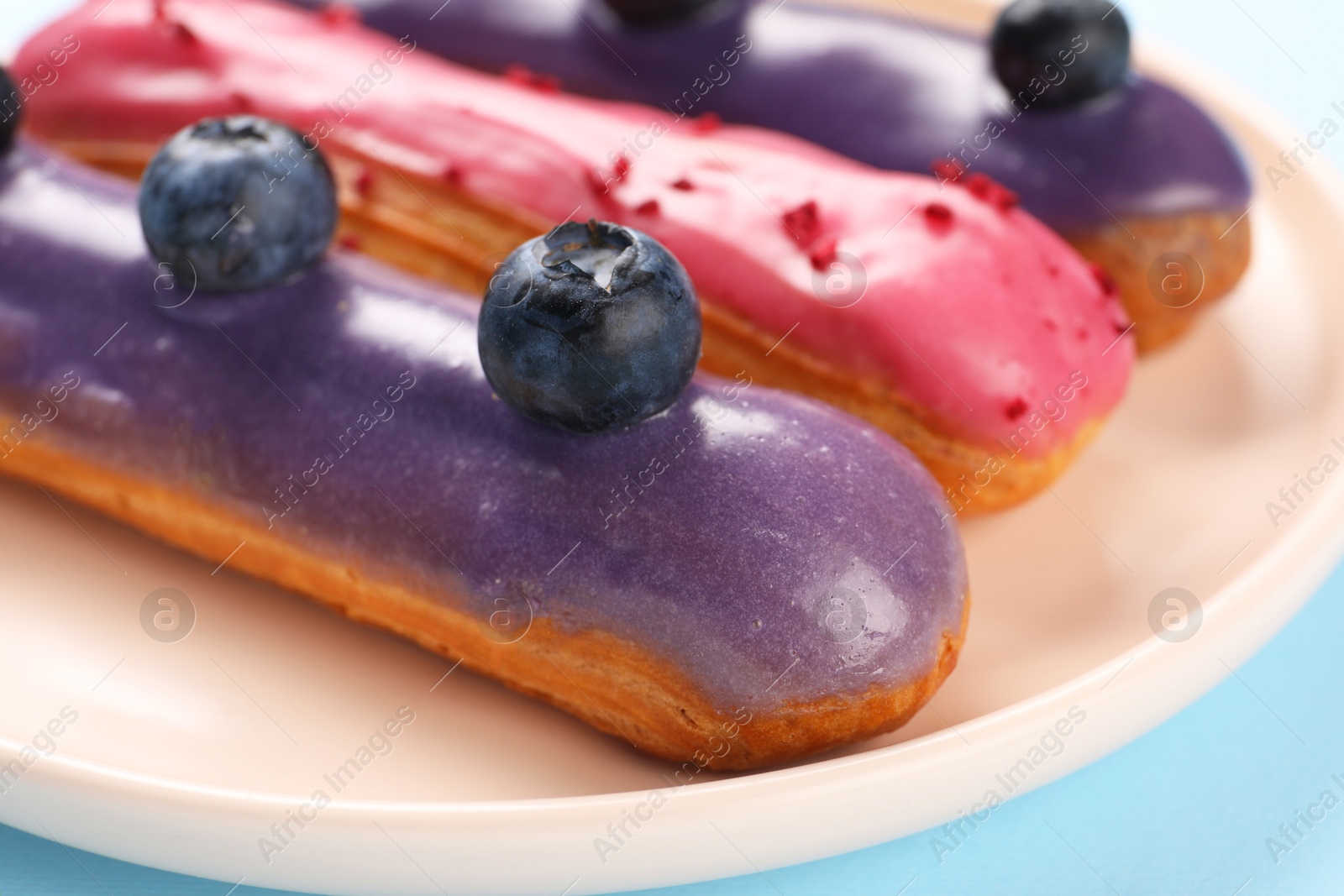 Photo of Delicious eclairs covered with glaze on light blue background, closeup