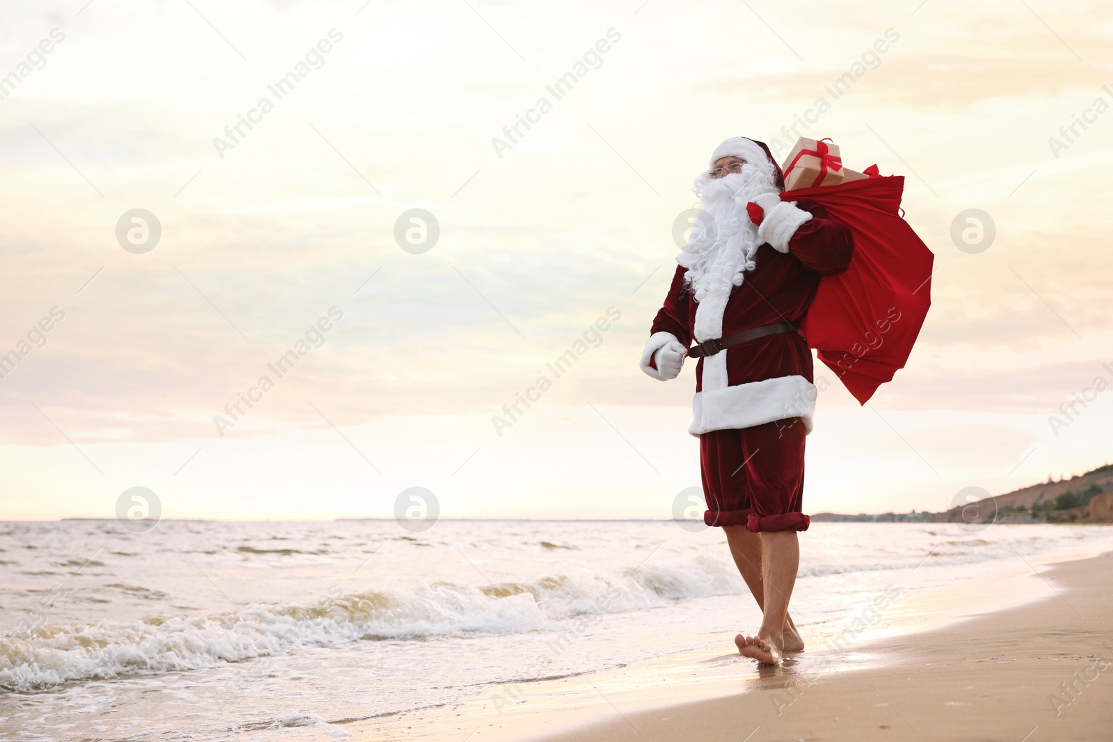 Photo of Santa Claus with bag of presents on beach, space for text. Christmas vacation