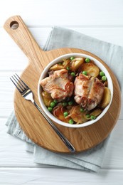 Tasty cooked rabbit with vegetables in bowl and fork on white wooden table, top view
