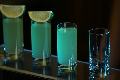 Photo of Shot glasses with alcohol drink and lime wedges on mirror surface, closeup