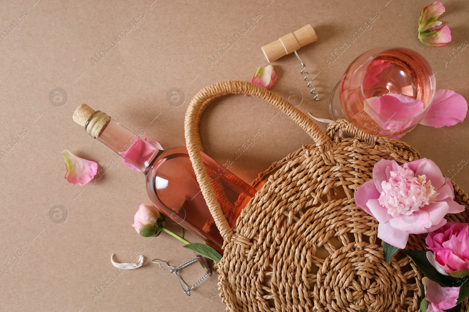 Photo of Flat lay composition with rose wine, wicker bag and beautiful pink peonies on brown background