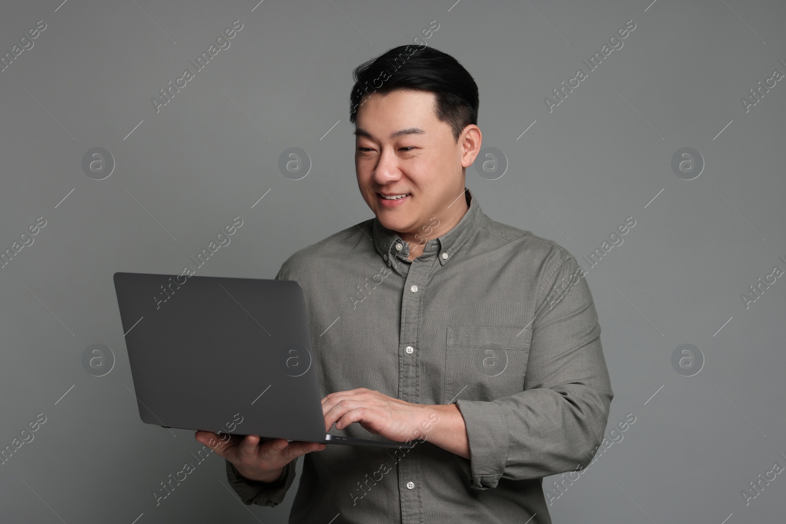 Photo of Portrait of happy businessman with laptop on grey background