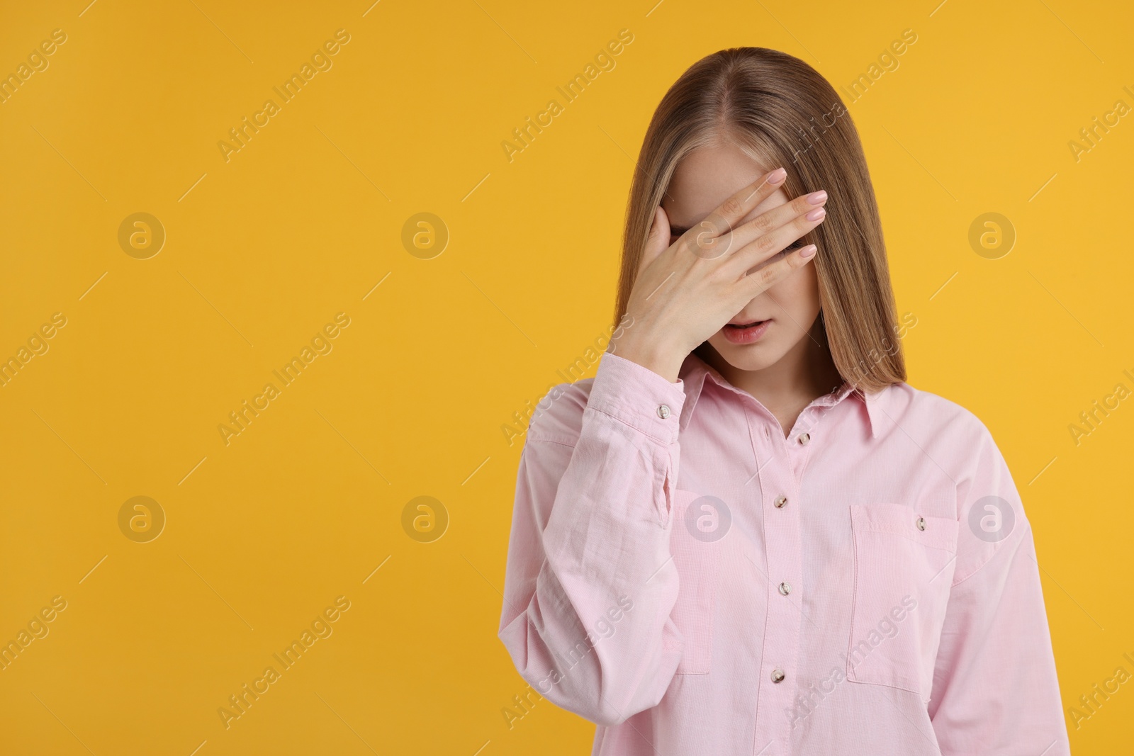 Photo of Embarrassed woman covering face with hand on orange background, space for text