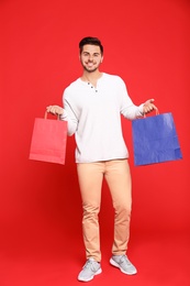 Photo of Full length portrait of young man with paper bags on red background