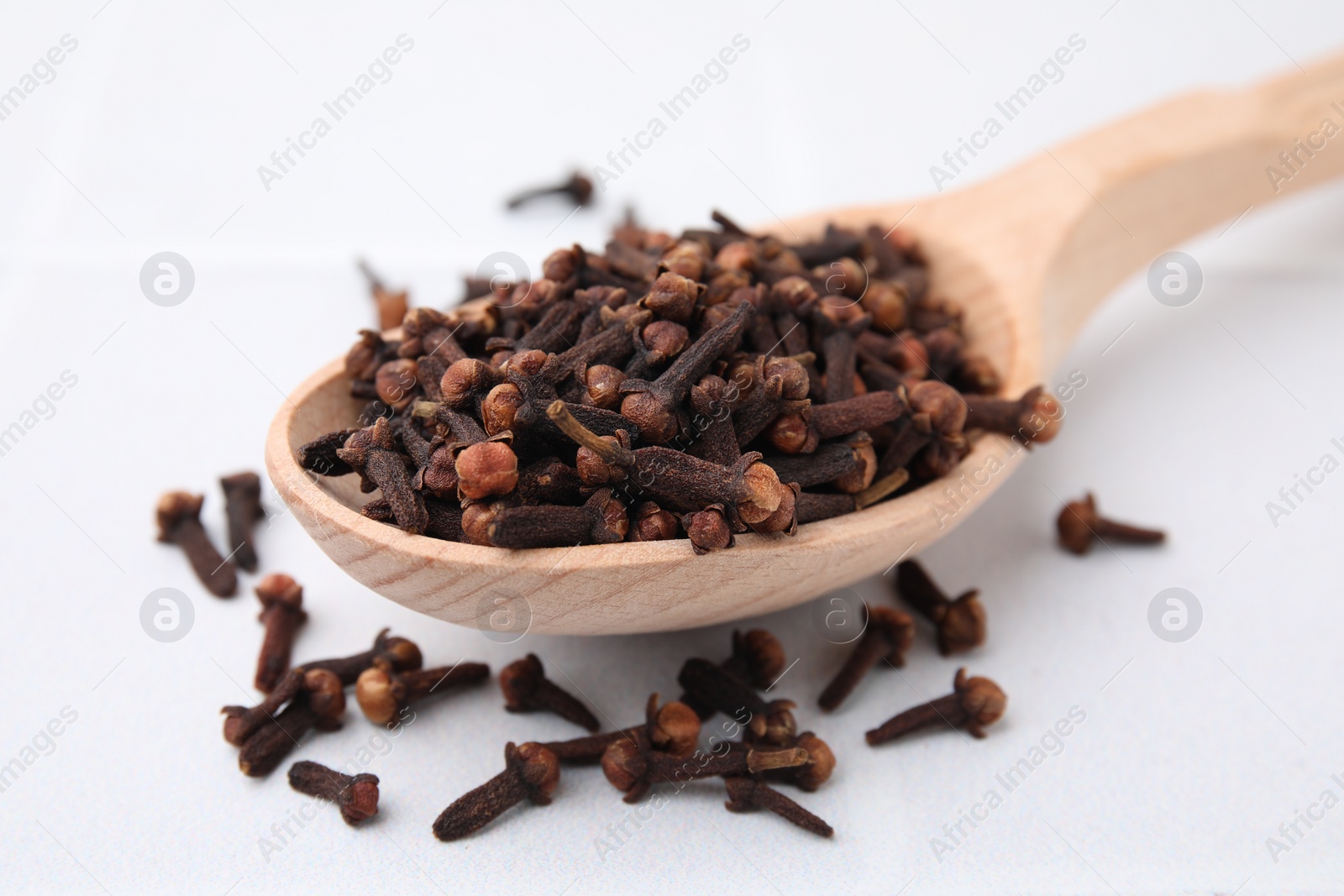 Photo of Spoon with aromatic dried clove buds on light table, closeup