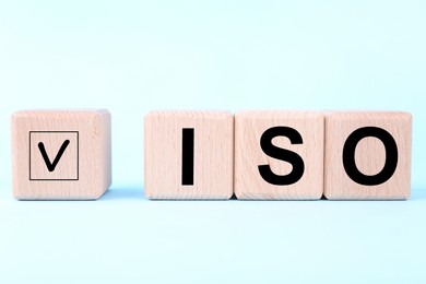 Photo of International Organization for Standardization. Wooden cubes with check mark and abbreviation ISO on light blue background