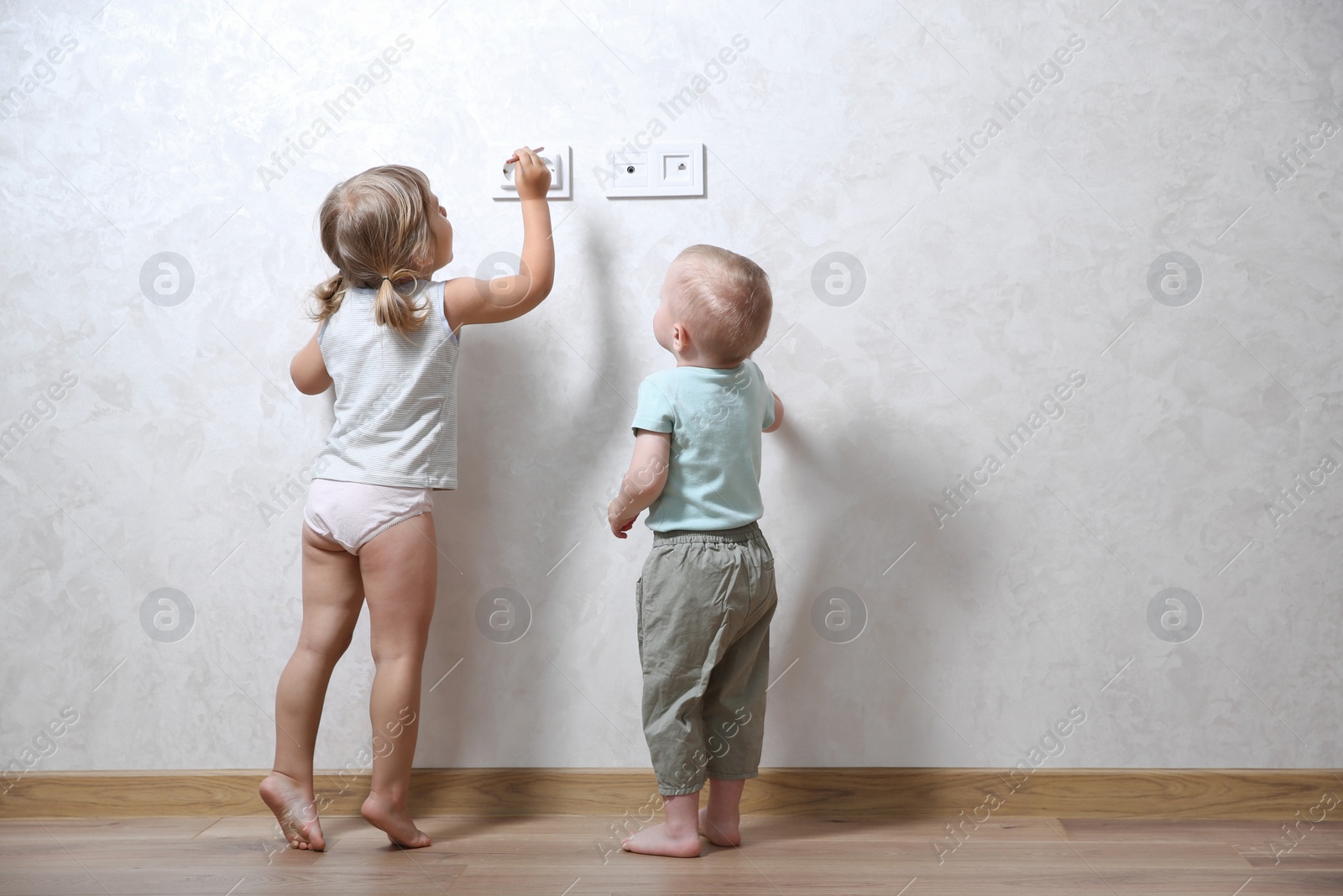 Photo of Little children playing with electrical socket indoors, space for text. Dangerous situation