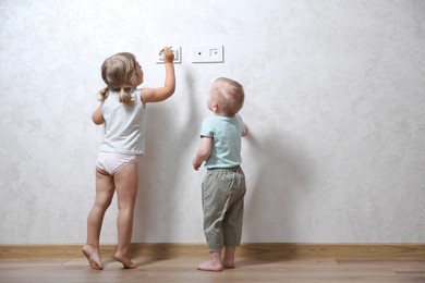 Photo of Little children playing with electrical socket indoors, space for text. Dangerous situation