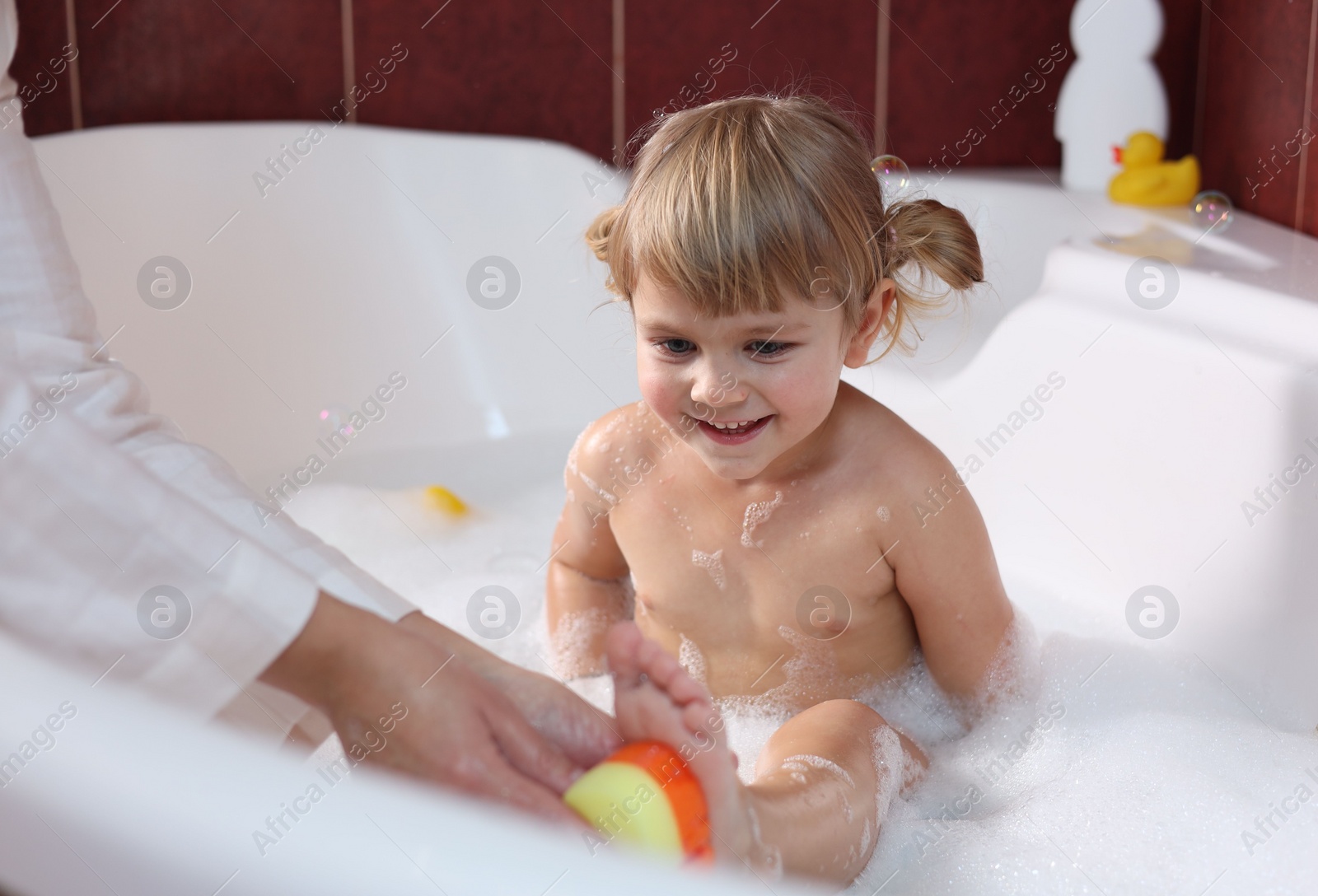 Photo of Mother washing her smiling daughter with sponge in bathtub, closeup