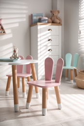 Photo of Small table and chairs with bunny ears in children's room interior