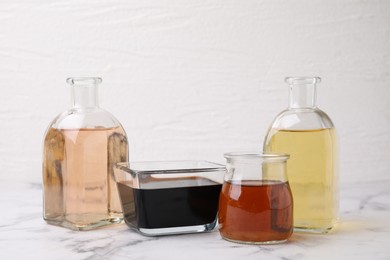 Photo of Different types of vinegar on light marble table, closeup