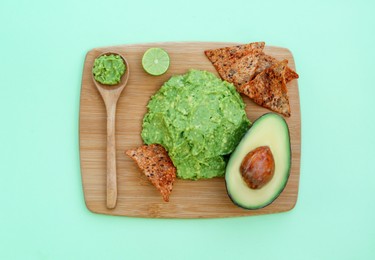 Delicious guacamole made of avocados, nachos and cut fruit on color background, top view