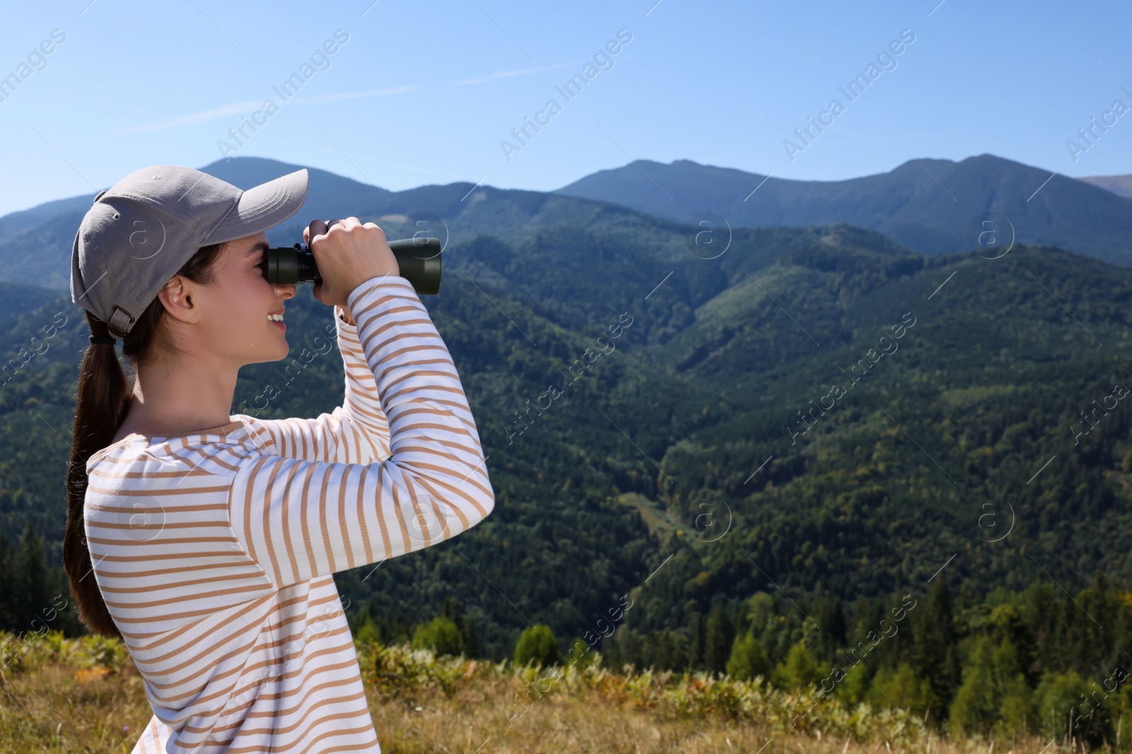 Photo of Woman looking through binoculars in mountains on sunny day