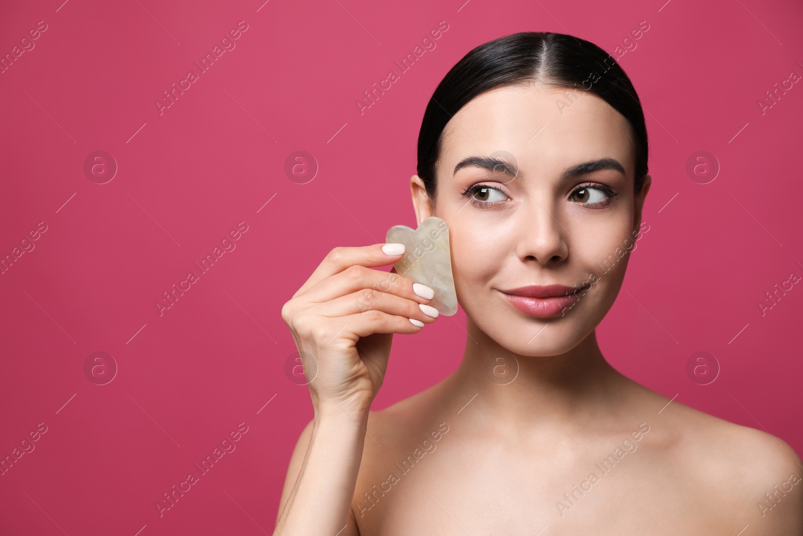 Photo of Beautiful young woman doing facial massage with gua sha tool on pink background. Space for text