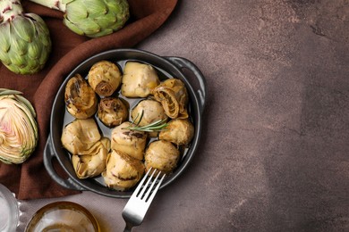 Delicious pickled artichokes with rosemary served on brown table, flat lay. Space for text