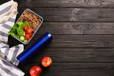 Flat lay composition with thermos and lunch box on black wooden background, space for text