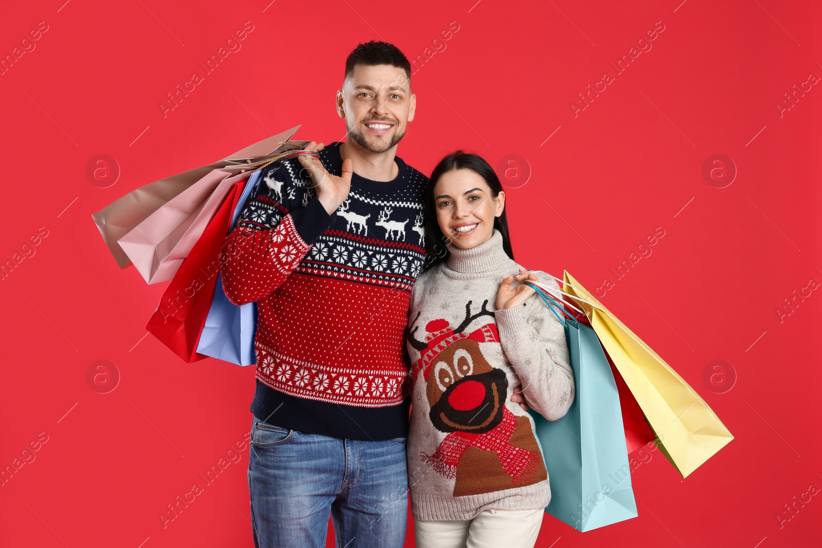 Photo of Happy couple with paper bags on red background. Christmas shopping