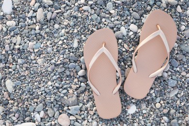 Photo of Stylish beige flip flops on pebble seashore, top view. Space for text