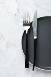 Stylish cutlery and plate on white marble table, top view