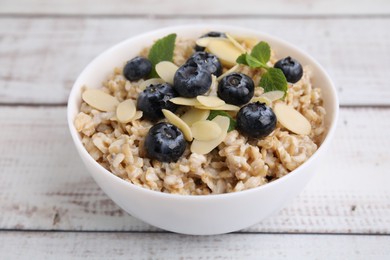 Photo of Tasty oatmeal with blueberries, mint and almond petals in bowl on wooden table, closeup