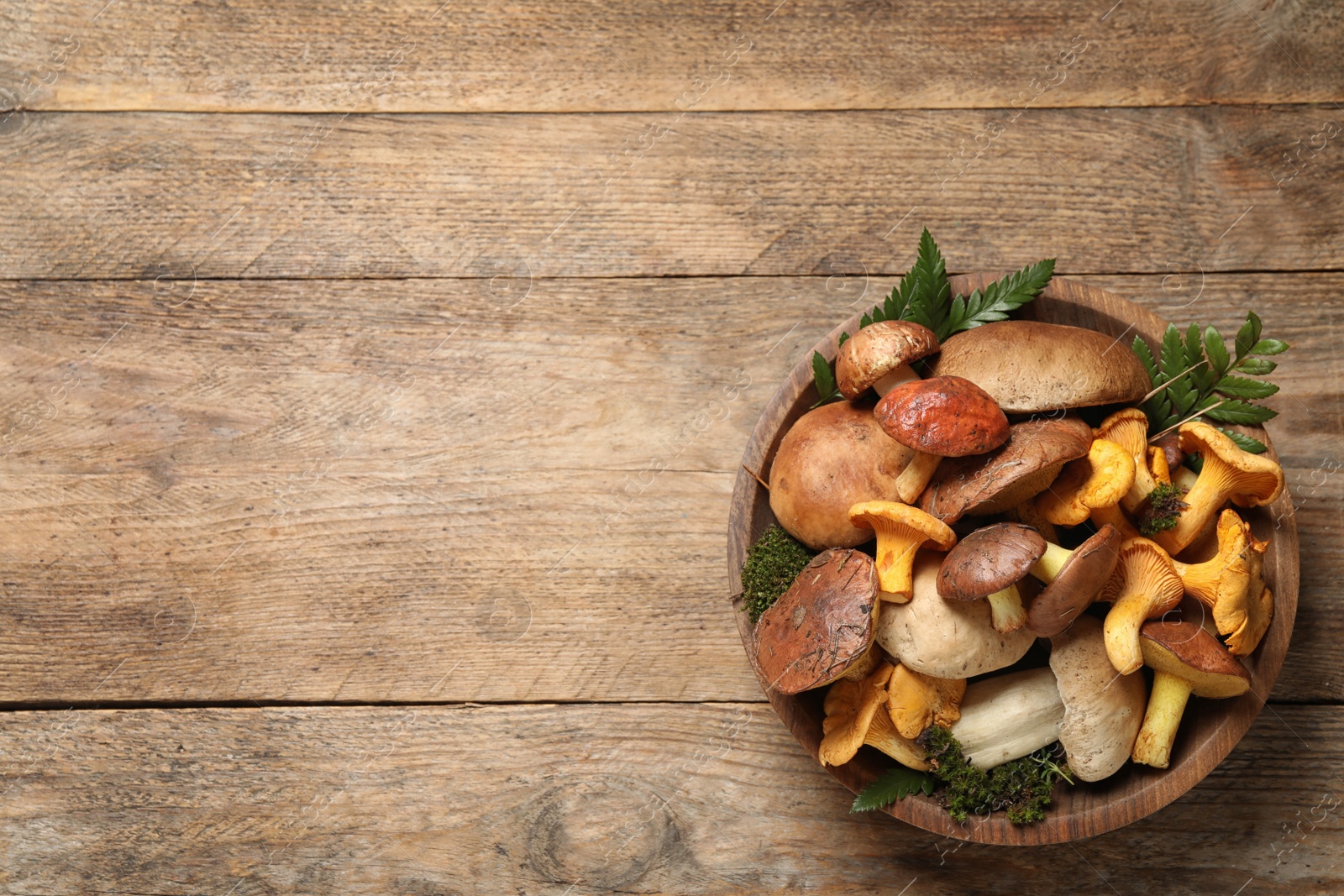 Photo of Bowl with different mushrooms on wooden table, top view. Space for text