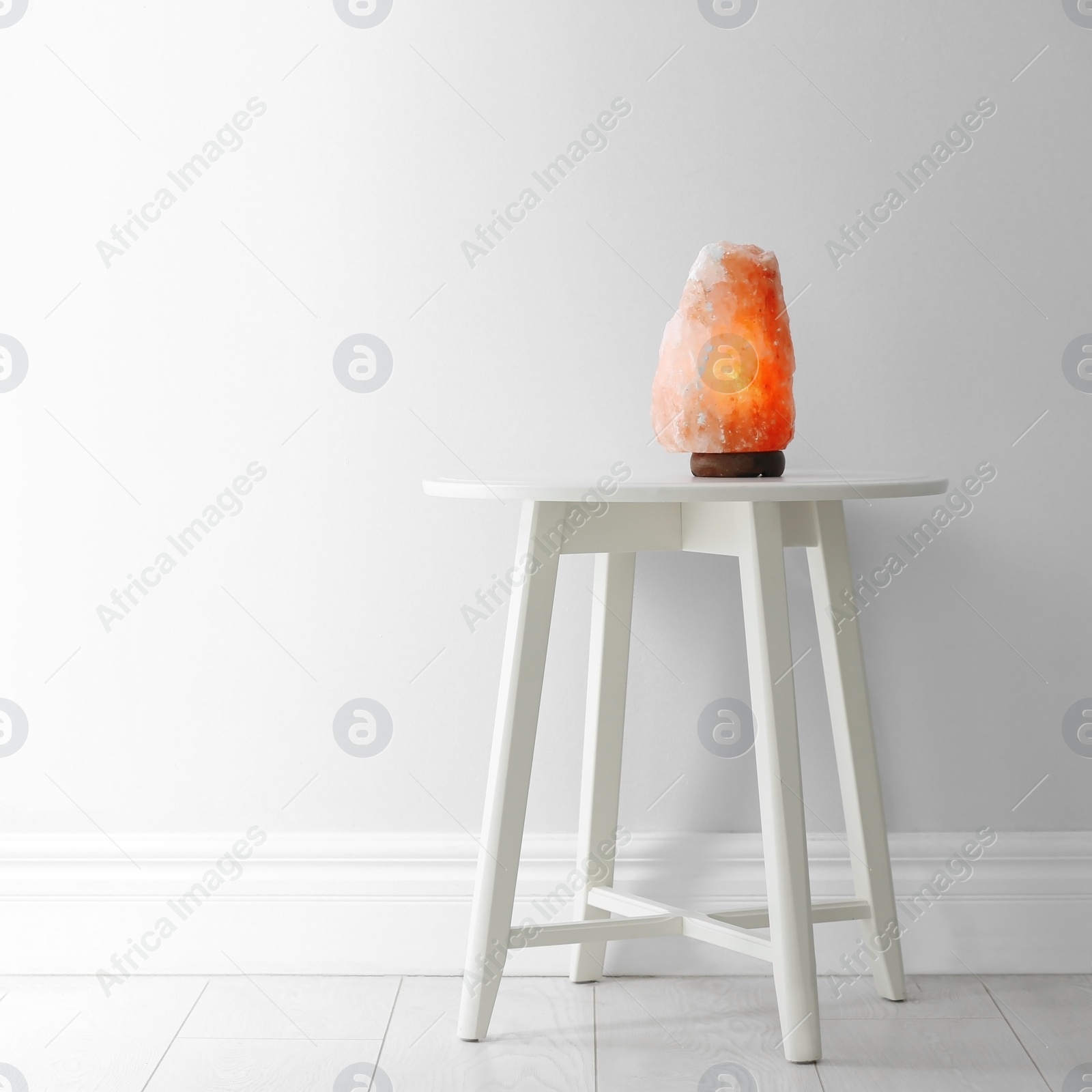 Photo of Himalayan salt lamp on table against  white wall. Space for text