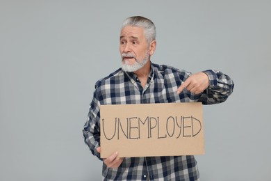 Photo of Senior man pointing at cardboard sign with word Unemployed on light grey background