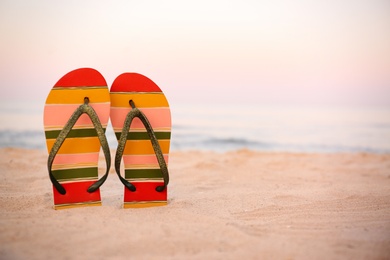 Photo of Stylish flip flops on sand near sea, space for text. Beach accessories