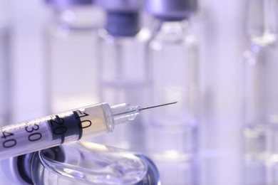 Photo of Glass vial and syringe with medication on white table, closeup. Space for text