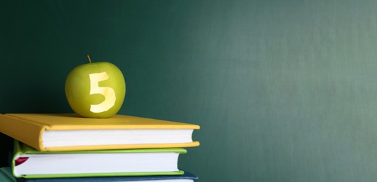 Image of Apple with carved number five as school grade on books near green chalkboard. Banner design with space for text