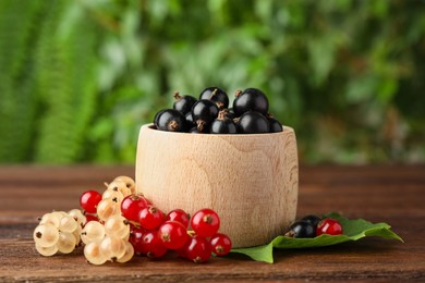 Photo of Different fresh ripe currants and green leaf on wooden table outdoors, closeup