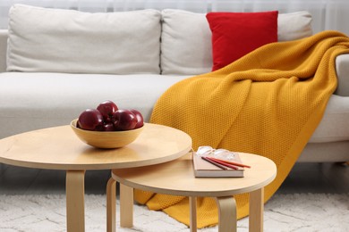 Photo of Red apples with book on nesting tables and comfortable sofa in living room. Interior design