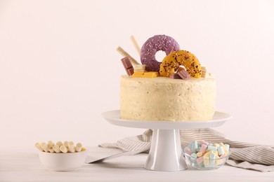Photo of Delicious cake decorated with sweets, wafer rolls and marshmallows on white wooden table, space for text