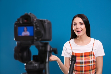 Young blogger with microphone recording video on camera against blue background