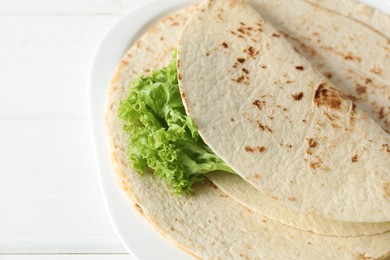 Tasty homemade tortillas and lettuce on white wooden table, closeup