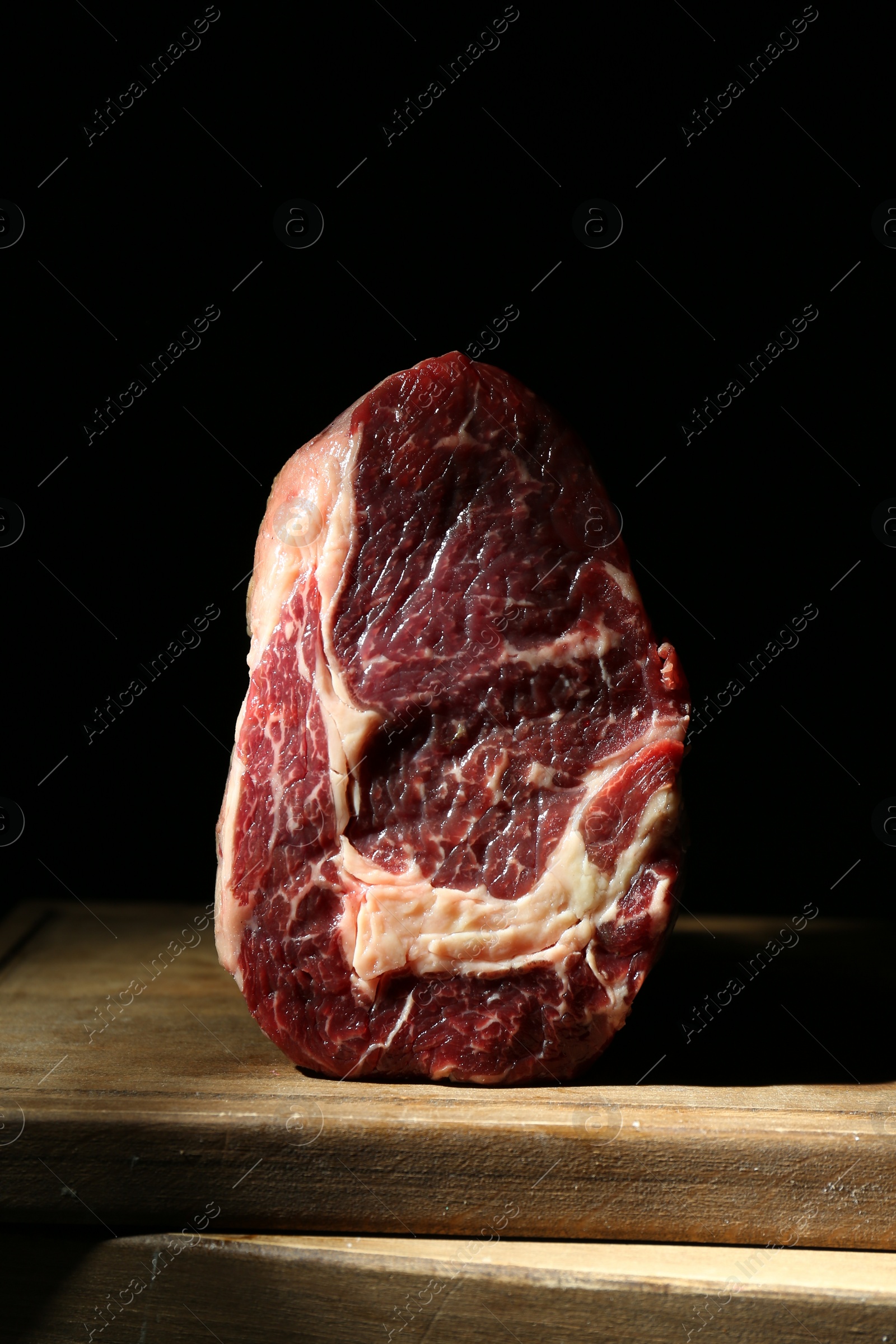 Photo of Piece of raw beef meat on wooden board against black background, closeup