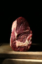 Piece of raw beef meat on wooden board against black background, closeup