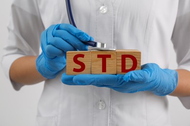 Doctor holding wooden cubes with abbreviation STD and stethoscope on white background, closeup