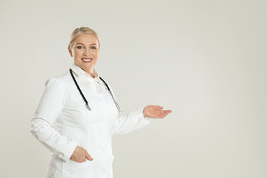 Portrait of mature doctor with stethoscope on light grey background. Space for text