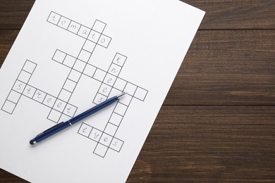 Crossword with answers and pen on wooden table, top view. Space for text