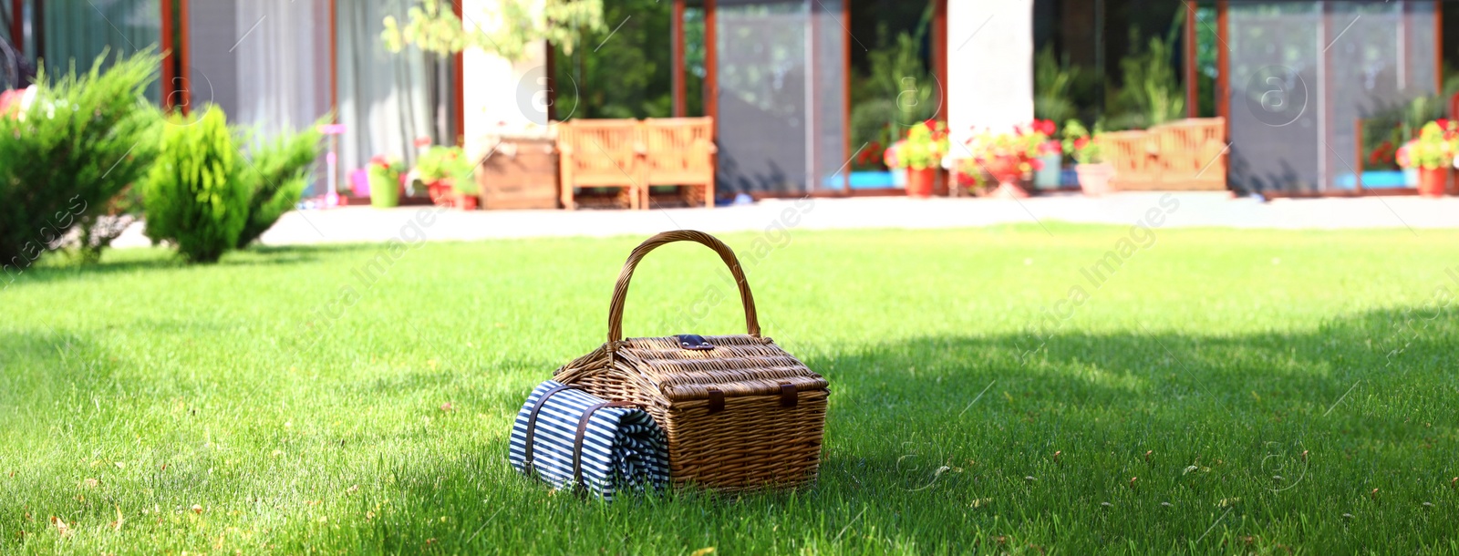 Image of Picnic basket with blanket on green lawn in garden. Banner design