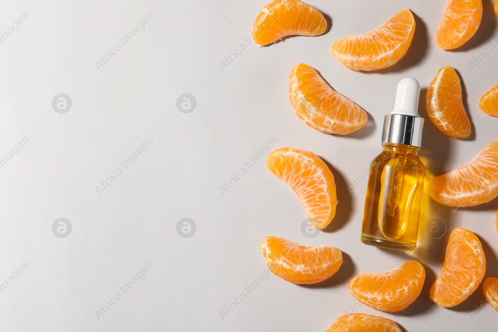 Photo of Aromatic tangerine essential oil in bottle and citrus fruit on grey table, flat lay. Space for text