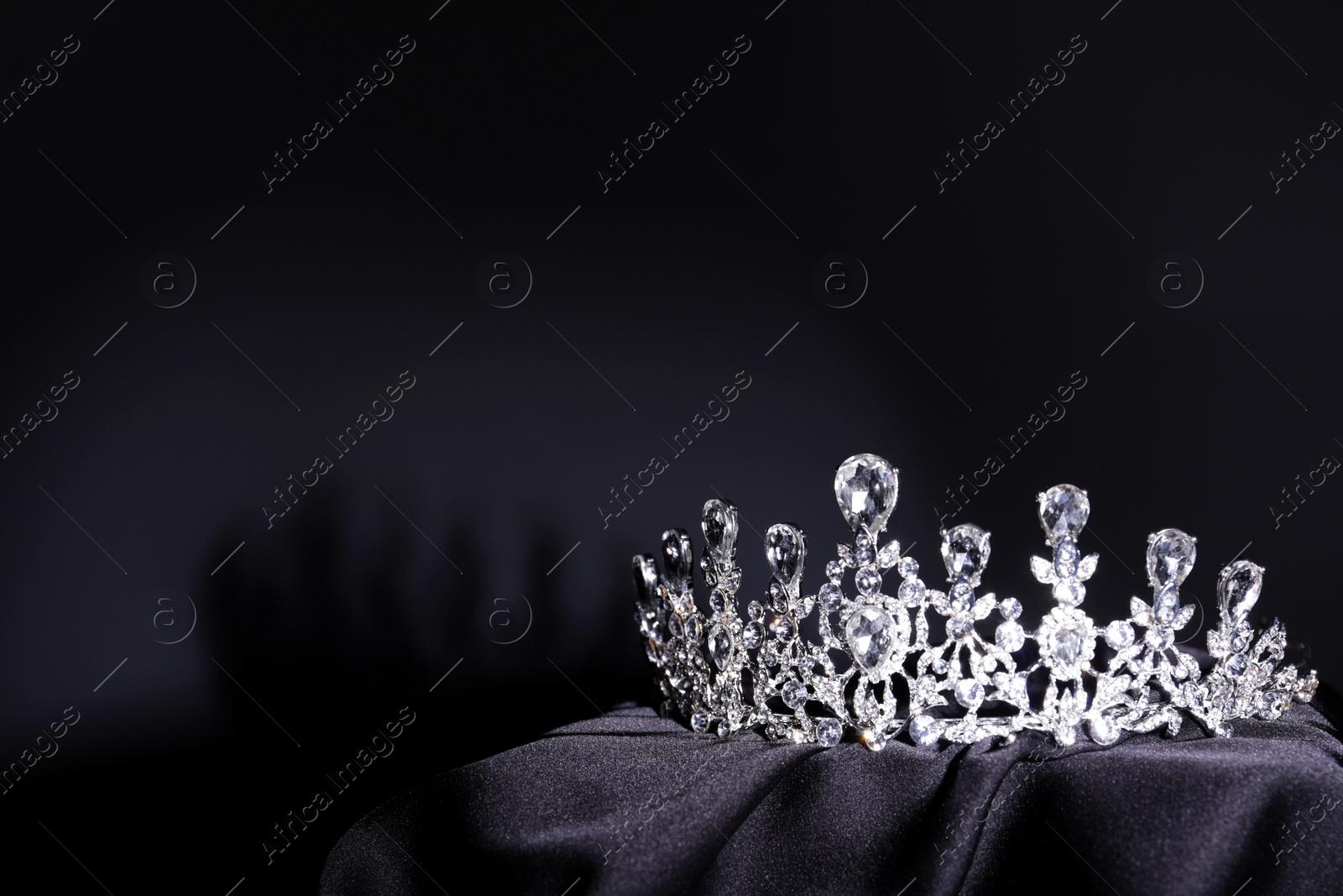 Photo of Beautiful silver tiara with diamonds on black cloth. Space for text