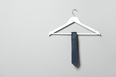 Photo of Hanger with blue necktie on light grey wall. Space for text