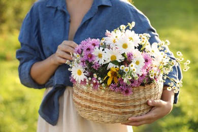 Photo of Woman holding wicker basket with beautiful wild flowers outdoors, closeup